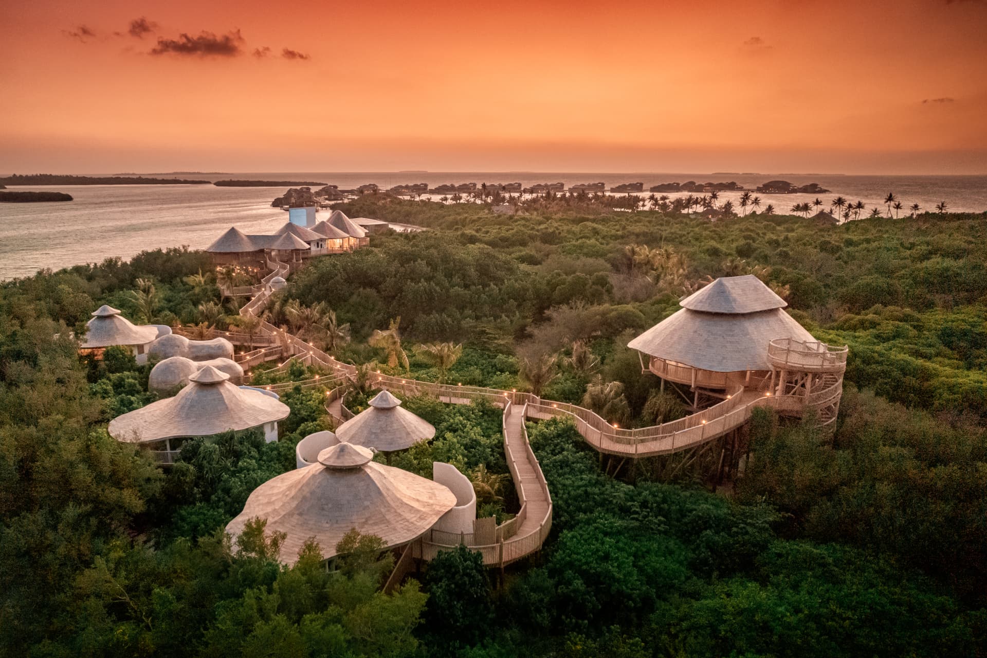 Overwater villas and treetop walkways at a Maldives resort during sunset